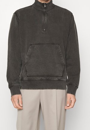 Sudadera de pelaje oscuro de algodón suave, con un cuello alto y media cremallera, bolsillo frontal tipo pouch y puños y dobladillo acanalados.