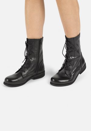 Black leather combat boots with lace-up front, side zipper, rounded toe, and flat heel. Smooth texture, ankle-high design, and minimal accents.