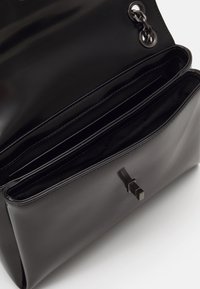 Borsa a tracolla in pelle verniciata nera con apertura superiore, che rivela due scomparti interni e una chiusura geometrica elegante.