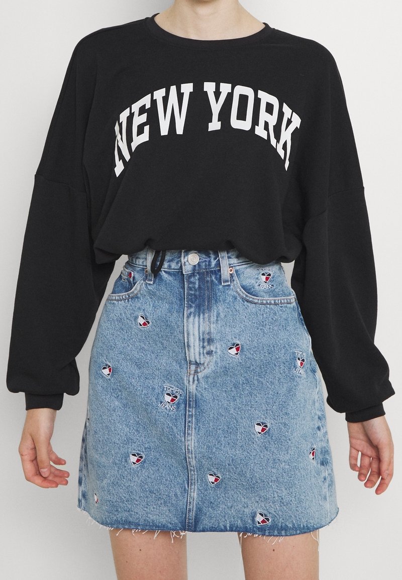 Czarna, oversize'owa bluza z białym napisem "NEW YORK", zestawiona z jasnoniebieską spódnicą dżinsową ozdobioną haftowanymi wzorami serc.