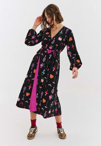 Czarna sukienka kopertowa z kolorowymi wzorami owoców, serc i akcesoriów. Posiada długie rękawy, pasek do wiązania oraz różowy panel akcentujący.