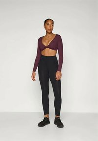 Bordó, hosszú ujjú crop top, csavart elöl, fekete leggingsszel és fekete sportcipőkkel párosítva. Simák és rugalmasak az anyaga.