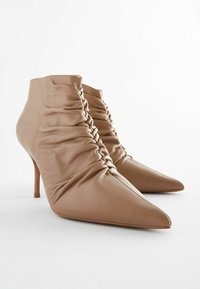 Bottes chelsea en cuir beige avec un design plissé, bout pointu et talon haut fin. Texture lisse avec des détails de couture le long des coutures.