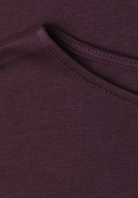 Gros plan d'un tissu tricoté violet foncé plié montrant des coutures détaillées et une texture.