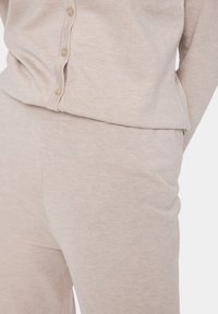 Ljusbeige lounge-set bestående av en knäpp-up topp med ribbat mönster och matchande byxor med sidfickor. Mjuk, stickad material.
