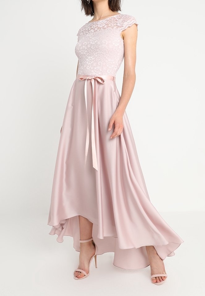 Femme portant un haut en dentelle rose pâle et une robe en satin à jupe asymétrique avec une ceinture en ruban et des sandales assorties à talons hauts.
