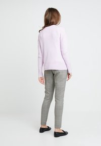 Pull en tricot violet clair avec ourlet côtelé, associé à un pantalon ajusté gris à carreaux. Des chaussures plates noires complètent la tenue.