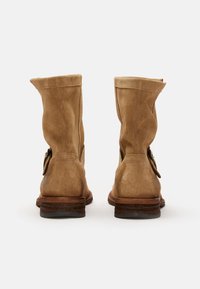Botas de tobillo de ante marrón con un diseño arrugado, que presentan un detalle de botón lateral y una puntera redondeada. Tacón de madera resistente y acabado texturizado.