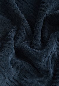 Coperta di colore blu scuro con tessuto morbido e peloso, caratterizzata da un sottile motivo geometrico, drappeggiata delicatamente per mostrare profondità e dettagli.