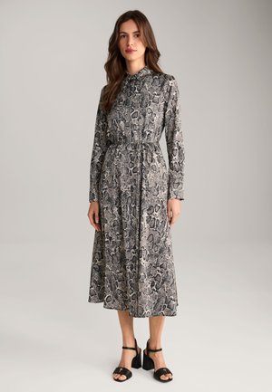 Langsleeve jurk in een zwart-wit slangenprint. Heeft een kraag, een strikceintuur en een vloeiende rok. Gecombineerd met zwarte blokhak sandalen.