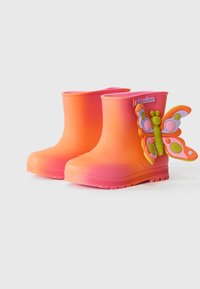 Bottes de pluie en caoutchouc roses et oranges avec un accent en forme de papillon sur le côté extérieur. Texture lisse et design à bout rond.