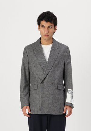 Gray houndstooth blazer with a double-breasted design, wide lapels, front pockets, and label detail on the sleeve. Smooth, textured fabric.