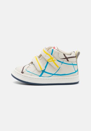 Baskets en cuir blanc avec des motifs géométriques bleus et jaunes, dotées de deux bandes Velcro, d'une pointe arrondie et d'une semelle en caoutchouc.