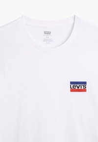 White short-sleeve t-shirt made of cotton, featuring a red, blue, and black "Levi's" logo patch on the left chest. Crew neck design.