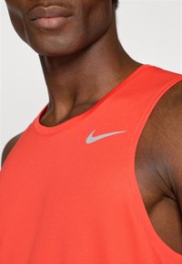 Piros Nike trikó, kerek nyakkivágással, sima anyagból készült. Kicsi szürke logó található a bal oldalon, a váll közelében.