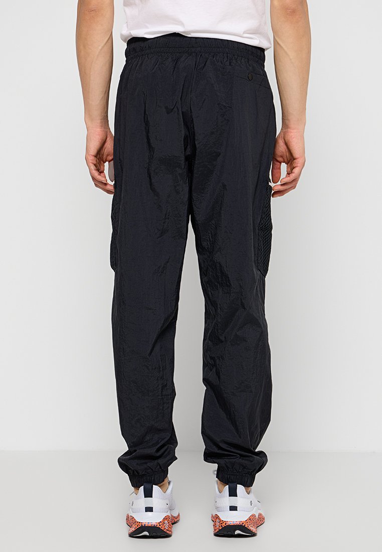 Pantaloni cargo neri, leggeri, in nylon con vita elastica, polsini a coste e tasche laterali. Dettaglio strutturato sui pannelli laterali.