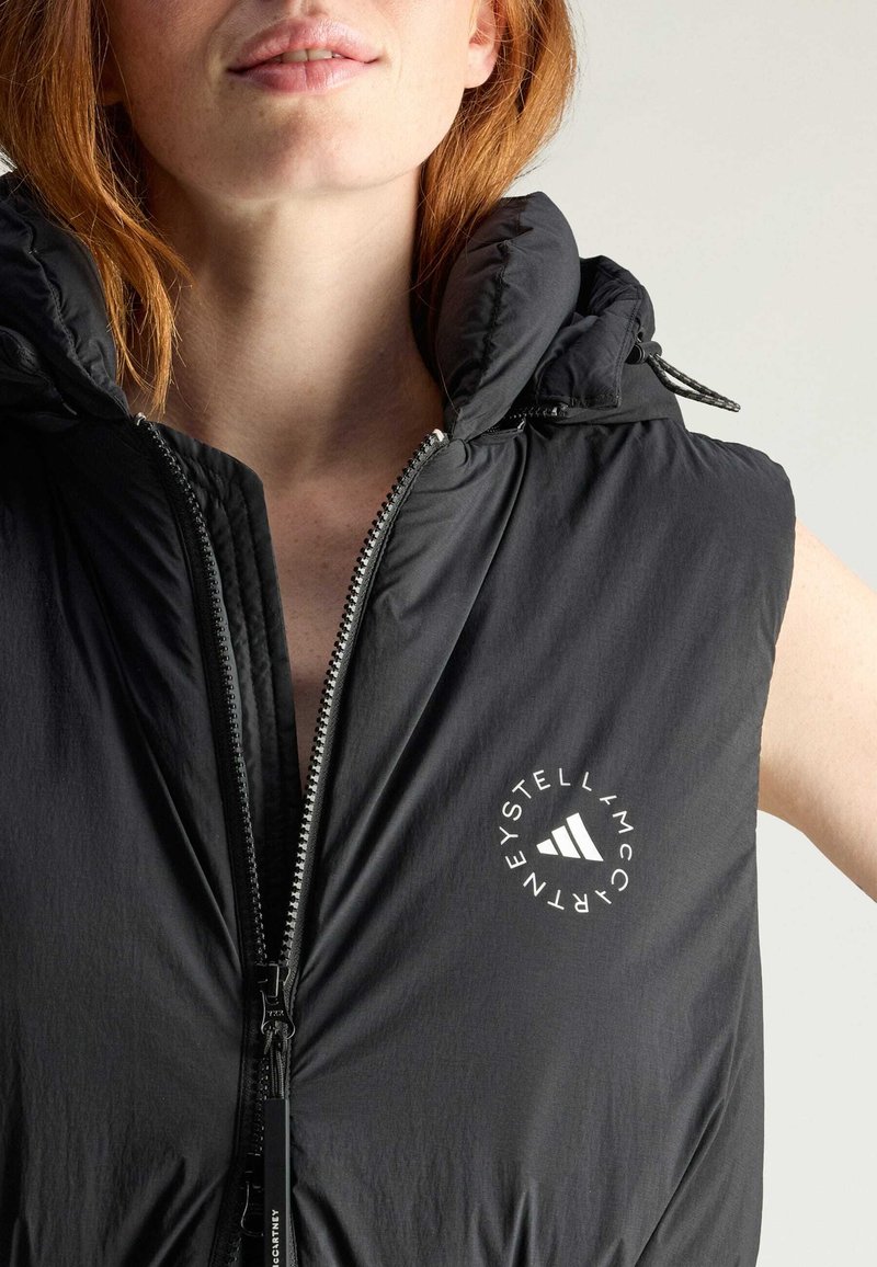 Zwarte mouwloze puffer vest met hoge kraag, rits sluiting en een logo aan de linkerkant. Stijlvolle textuur, lichtgewicht materiaal.