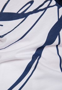 White fabric top featuring a navy blue abstract design with smooth texture and sparkling accents along the neckline.