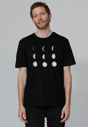 Schwarzes T-Shirt mit einem grafischen Druck der Mondphasen in Weiß, der unterschiedliche Formen und Texturen im Brustbereich zeigt.