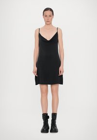 Rochie neagră, fără mâneci, cu decolteu tip cowl, având o croială lejeră și slituri laterale. Asortată cu ghete de tip combat, mascate, negre.