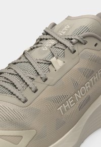 Κοντινό πλάνο αθλητικού παπουτσιού The North Face σε μπεζ χρώμα με υφασμάτινη υφή, διασταυρούμενα κορδόνια και λογότυπο της μάρκας στο πλάι.