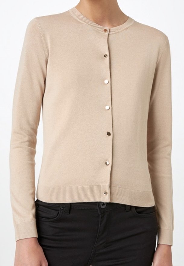 Cardigan beige à manches longues avec boutons et col rond porté sur un pantalon noir, vue rapprochée du torse.