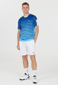 Blå och vit idrottsdräkt med en randig t-shirt med kort ärm och vita shorts, märkta med 'FZ', i kombination med svarta och vita sneakers.