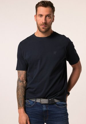 Camiseta de algodón azul marino con cuello redondo, mangas cortas y un logo sutil en un color contrastante cerca del pecho, combinada con jeans de mezclilla y un cinturón estampado.