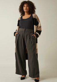 Overmaatse zwart en beige gestreepte cardigan over een donkere top en hoog-gewijde grijze wijde broek met zijzakken en verfijnde textuur.