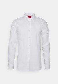 Biała koszula z długim rękawem z przodu zapinana na guziki, wykonana z gładkiej tkaniny. Posiada klasyczny kołnierzyk i jednolity wzór, z czerwoną metką.