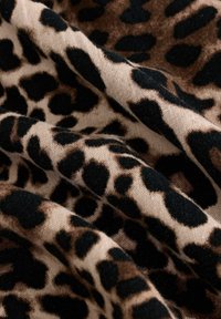 Leopardikuosis, jossa on vaalea beige pohja suurilla mustilla ja ruskeilla laikkuilla, esittelee pehmeää rakennetta ja laskostunutta ilmettä.