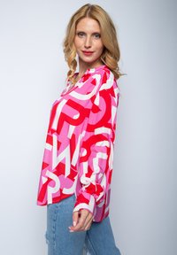 Langärmlige Bluse in Pink und Rot mit kräftigen weißen Buchstaben, aus leichtem Stoff gefertigt, entspannter Schnitt und mit Knopfmanschetten.