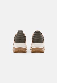 Sneaker marroni e verde scuro con talloni imbottiti, suole intermedie bianche e suole esterne in gomma testurizzata, dotati di un design con lacci e accenti discreti.