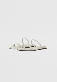 Lys grå flate sandaler med tynne stropper og en glatt såle, laget av gummiaktig materiale med et minimalistisk design.