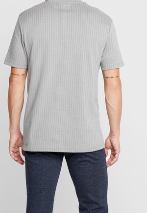 Grå ribbet t-shirt med korte ærmer, rund halsudskæring og en let forlænget bagkant. Brugt sammen med teksturerede marineblå bukser.