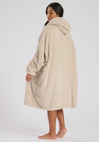 Rocchetto con cappuccio beige e texture a onde. Realizzato in materiale morbido, presenta maniche lunghe e una vestibilità oversize, che arriva a metà polpaccio.