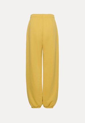 Kollased sportpüksid, millel on lahtine lõige, elastne vöökoht ja elastsed sääreosad. Valmistatud pehmest, tekstureeritud kangast.