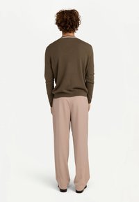 Olivgrön stickad tröja med åtsittande muddar, kombinerad med löst sittande ljusrosa byxor. Mjuk textur med subtila veck och rena linjer.