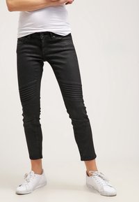 Svarta slim-fit jeans med ribbad texturering vid knäna, gjorda av denim. Bärs med vita sneakers som har en kortad fotleddesign.