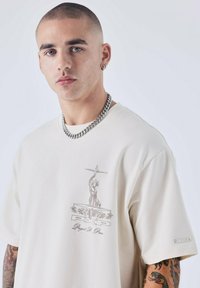 Beige graphic t-shirt met een zilveren print van een standbeeld en de tekst "PXP." Gladde textuur, oversized ontwerp, korte mouwen en gestikte labeldetails.