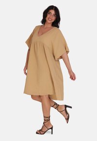 Robe beige, à coupe ample, en tissu texturé avec un décolleté en V et des manches courtes, présentant une silhouette évasée et une longueur à mi-genou.