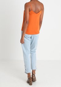Orange satin camisole med tunna band, kombinerad med ljusblå denimbyxor med fransar i nederkant och sidodetaljer. Bruna klackar med ormskinnsmönster.