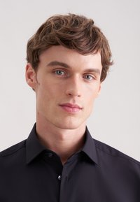 Czarna koszula na guziki wykonana z gładkiej tkaniny. Posiada klasyczny kołnierzyk, guziki z przodu oraz dopasowany krój. Prosty design bez wzorów.