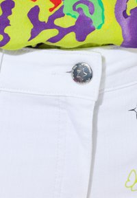 Valkoinen denimi vyötäröosa, jossa on hopeinen nappi, joka esittää tähteä. Näkyvä ompelu ja brodeerattu design, joka sisältää keltaisen perhosen.