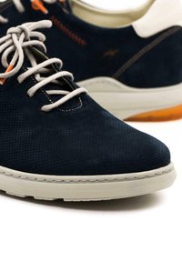 Zapatos de ante azul marino con una superficie texturizada, suela de goma crema, cordones gris claro y detalles en naranja en los ojetes.