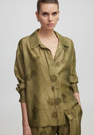 Chemise olive-verte à boutons en tissu léger et texturé avec des motifs floraux. Dotée d'un col classique et de manches retroussables.