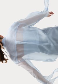 Blusa leggera azzurro chiaro, con maniche lunghe, caratterizzata da una vestibilità ampia e tessuto trasparente. Accentuata con un bordo azzurro chiaro lungo i lati.