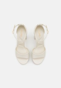 Sandali beige con tacco, dotati di sottile cinturino alla caviglia e ampia fascetta anteriore. Texture liscia e design minimal con un discreto logo del brand sulla soletta.