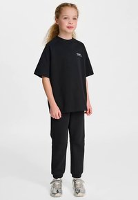 Svart bomullst-shirt med korta ärmar och rund halsringning, kombinerad med matchande svarta joggingbyxor. Inkluderar en liten logotypdetalj på bröstet.