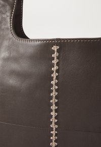 Dark brown leather tote bag featuring a smooth texture and decorative beige stitching along the seam, with a simple, open top design.